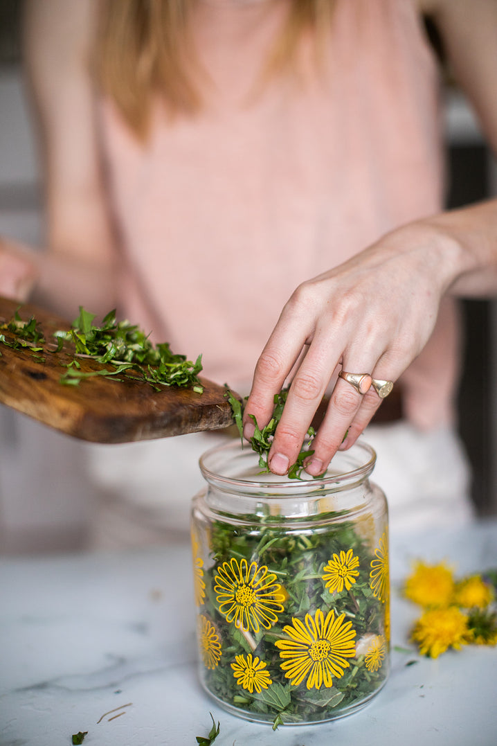 hands emptying the chopped herb contents of a cutting board into a jar.a glass
