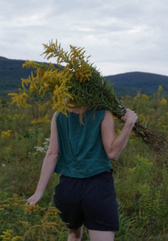 the back of a woman holding a bouquet of goldenrod over her shoulder, walking up a hill.